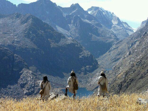 Tres hombres arhuacos de blanco frente a una laguna entre picos de alta montaña